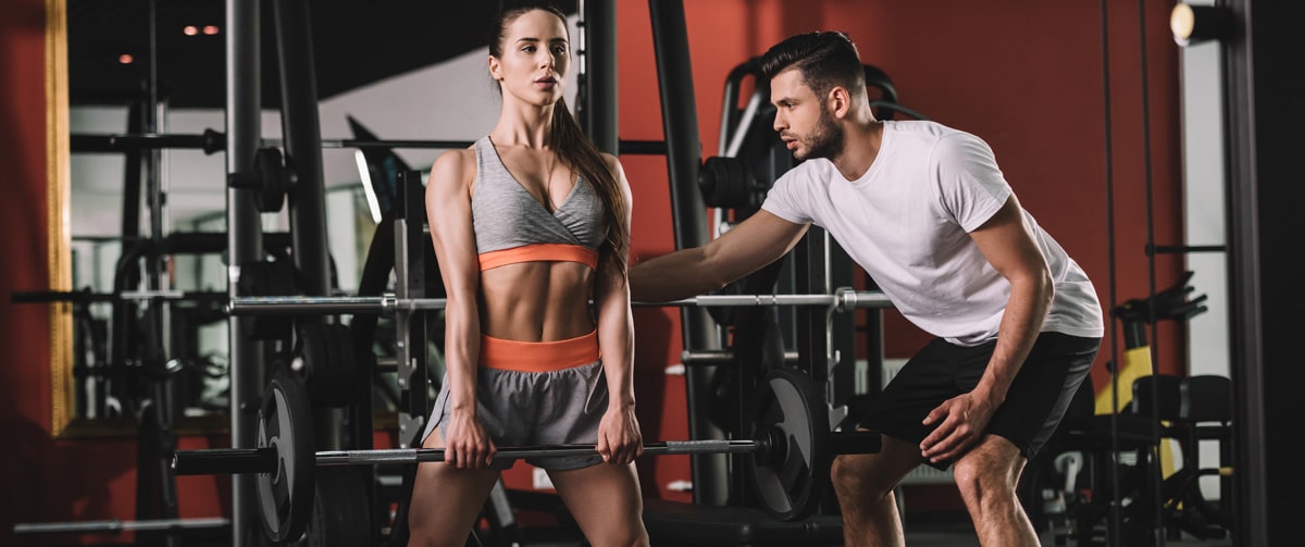 fitness-trainer-supporting-fit-woman-lifting-barbells